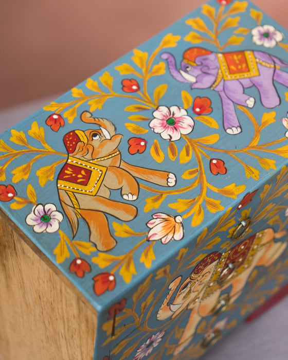 Decorative turquoise box with colourful elephant illustrations on a wooden surface