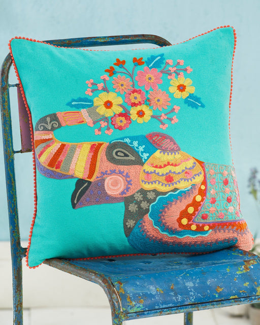 Colourful embroidered pillow with an elephant design on a blue chair against a light blue background
