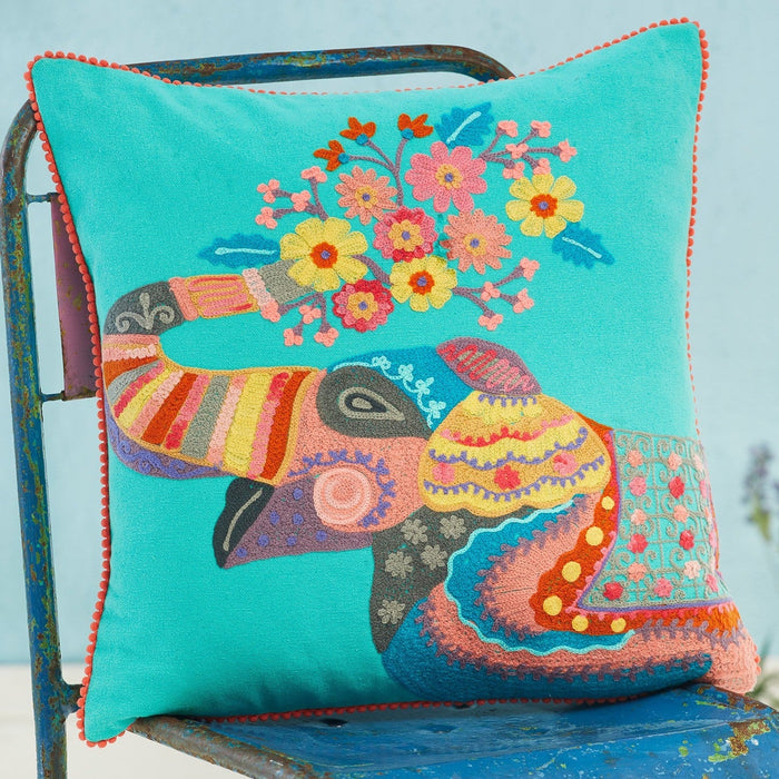 Colourful embroidered pillow with an elephant design on a blue chair against a light blue background