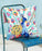 Colorful pillow with peacock design on a blue chair against a light blue wall.