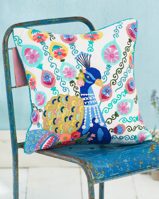 Colorful pillow with peacock design on a blue chair against a light blue wall.