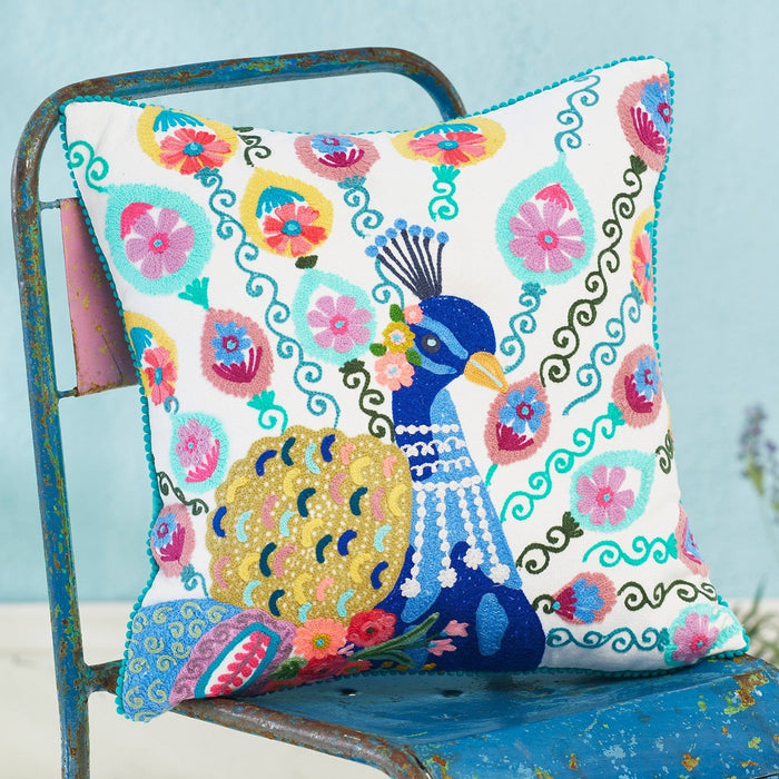 Colorful pillow with peacock design on a blue chair against a light blue wall.