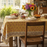 Dining table set with a yellow floral tablecloth, fruit, and flowers in a sunlit room.
