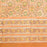 A close-up of a peach-colored fabric tablecloth with an all-over floral block print in green, yellow, and brown.  There is a triple layer border and the fabric is edged with coordinating striped ticking.