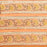 A close-up of a peach-colored fabric tablecloth border with an all-over floral block print in green, yellow, and brown