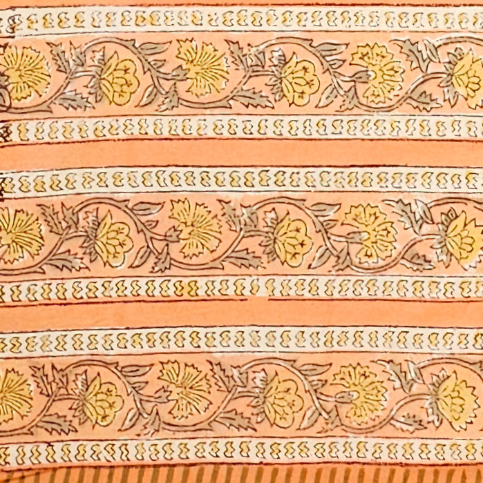 A close-up of a peach-colored fabric tablecloth border with an all-over floral block print in green, yellow, and brown