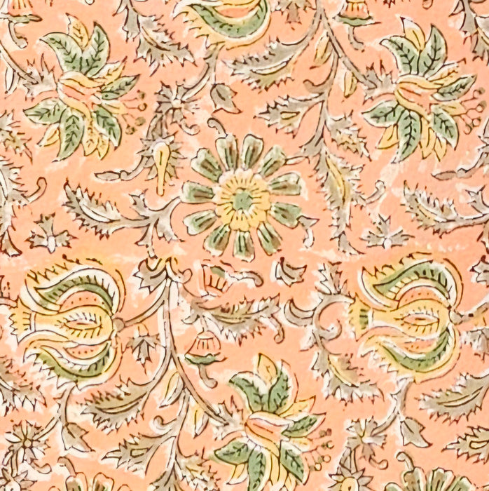 A close-up of a peach-colored fabric tablecloth with an all-over floral block print in green, yellow, and brown