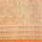 A close-up of a peach-colored fabric tablecloth with an all-over floral block print in green, yellow, and brown, featuring a wide decorative border.