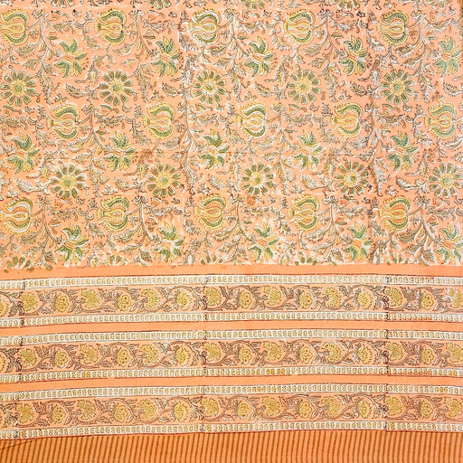 A close-up of a peach-colored fabric tablecloth with an all-over floral block print in green, yellow, and brown, featuring a wide decorative border.