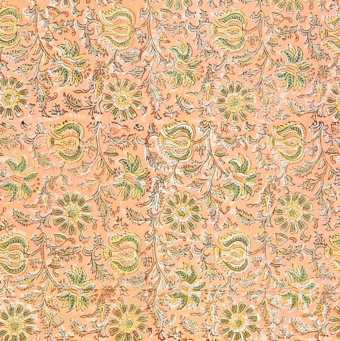 A close-up of a peach-colored fabric tablecloth with an all-over floral block print in green, yellow, and brown