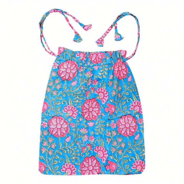 A drawstring bag for a pair of pyjamas with a pink-and-green block-print floral design against a vibrant turquoise blue background, laid flat against a white background.