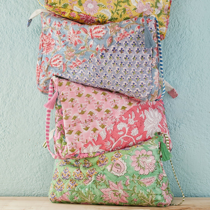 Stack of colourful block-printed fabric bags with floral patterns  set against a light blue wall