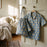 A light blue short-sleeve button-up pyjama set and matching drawstring bag with a beige and brown circular floral pattern hang on a wooden hanger and a door hook in a softly lit bedroom.