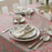 Elegant table setting with a floral pink lily block print tablecloth, plates, cups, and silverware.