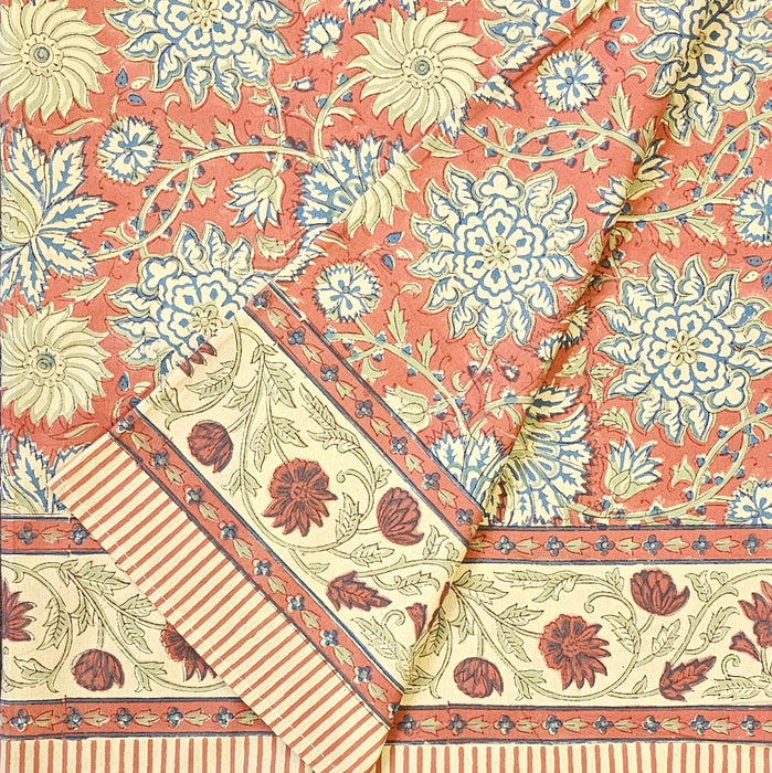 Folded terracotta rust and slate blue hand-block printed botanical themed cotton tablecloth with ticking-stripe edge.