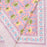 A close-up of a pink printed textile with a floral and vine pattern in yellow, green, and light blue, finished with a decorative border.