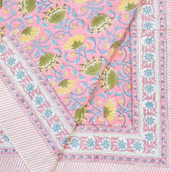A close-up of a pink printed textile with a floral and vine pattern in yellow, green, and light blue, finished with a decorative border.