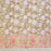 A section of a hand-block-printed tablecloth features a repeating floral and leaf motif in pink, white, and brown against a warm camel background, with a decorative border along the bottom.