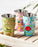 Three colourful hand-painted stainless steel and enamel tumblers with floral designs on a wooden surface