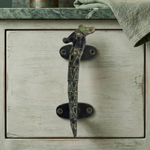 Decorative seahorse design brass cabinet handle on a wooden drawer with a marble countertop in the background