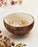 Coconut shell bowl with floral patterns on a light background with cardamom pods.