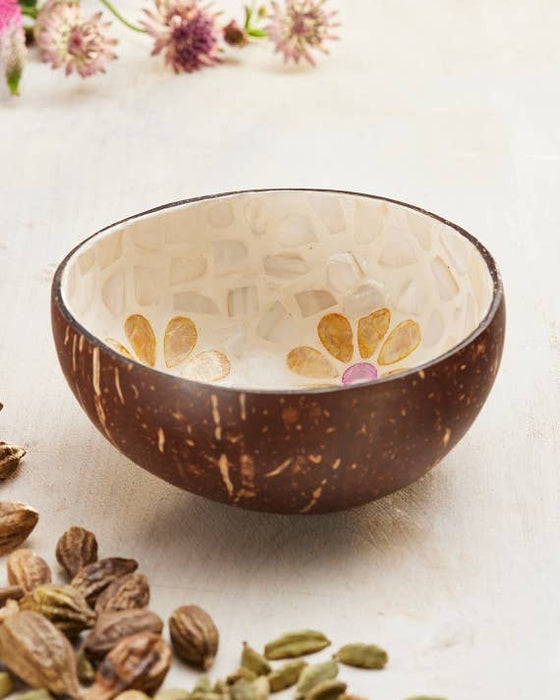 Coconut shell bowl with floral patterns on a light background with cardamom pods.