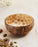 Coconut shell bowl with honeycomb pattern on a light wooden surface with cardamom pods.