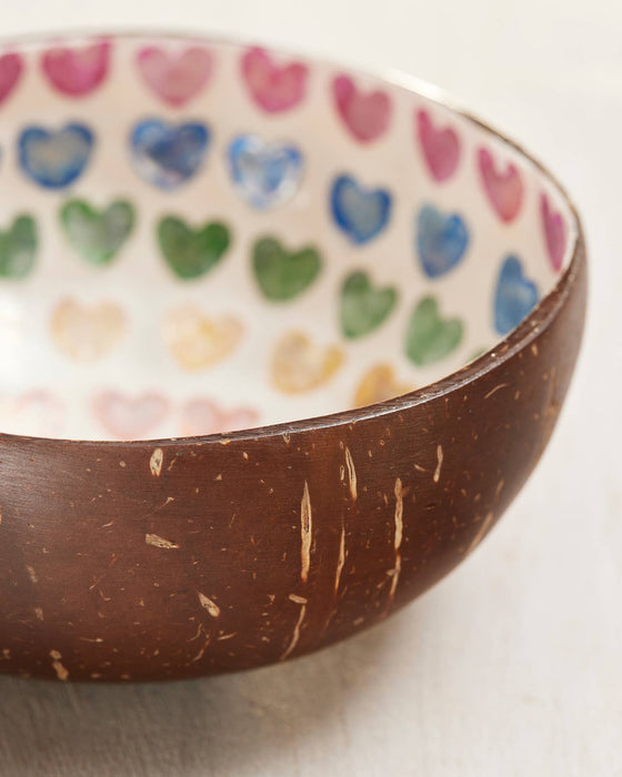 Coconut shell bowl with colorful heart pattern inside on a light background