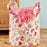 Floral-patterned laundry basket with a pink towel on a wooden surface.