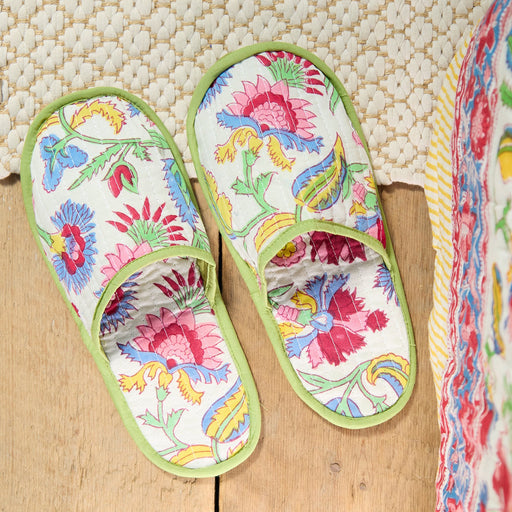 Colorful floral-patterned slippers on a wooden surface with a textured white background.