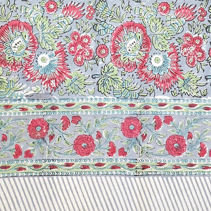 Handcrafted 100% cotton tablecloth in Slate Garden print, showing crimson red flowers, sage green leaves on a blue-grey background, and matching striped hem detail.