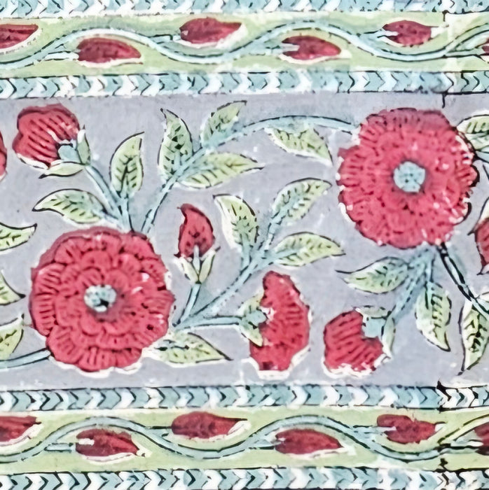 Detailed image of the border of the Handcrafted 100% cotton tablecloth in Slate Garden print, showing crimson red flowers, sage green leaves on a blue-grey background.