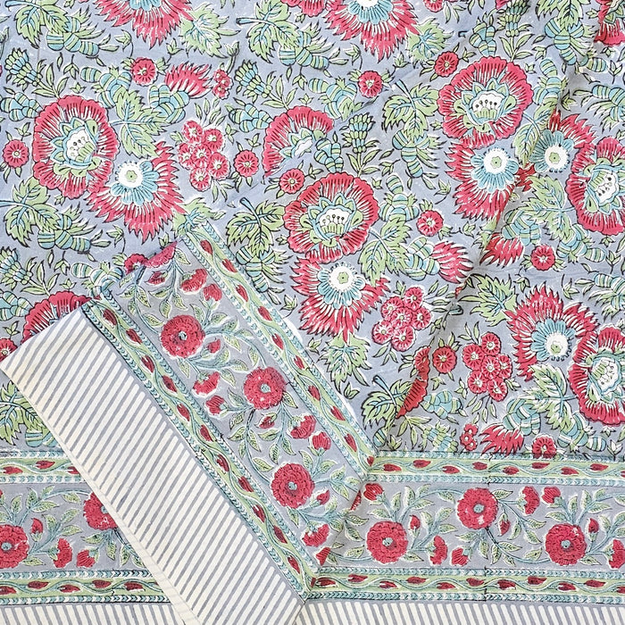 Handcrafted 100% cotton tablecloth in Slate Garden print, showing crimson red flowers, sage green leaves on a blue-grey background, and matching striped hem detail.  Folded back.