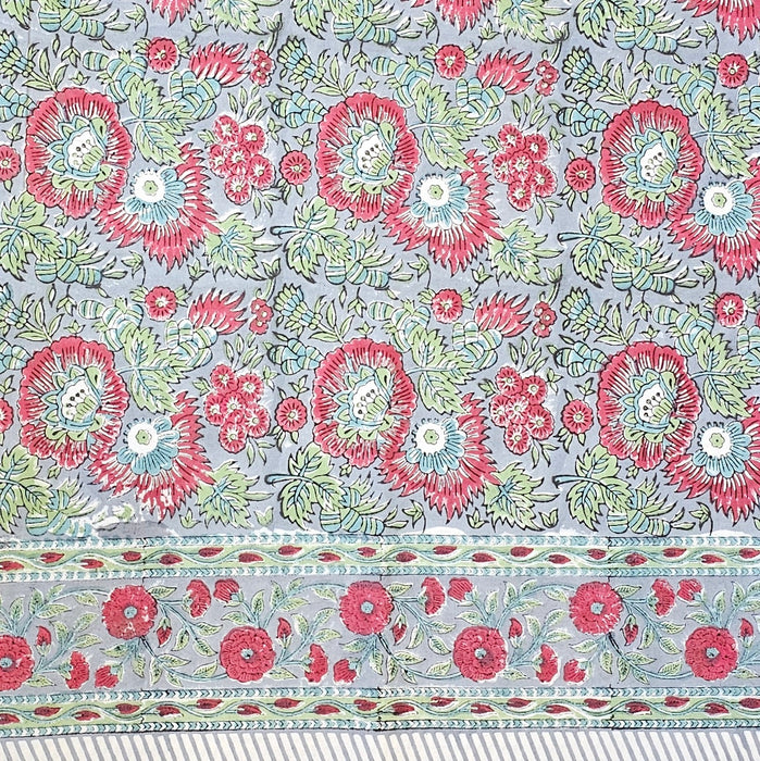 Handcrafted 100% cotton tablecloth in Slate Garden print, showing crimson red flowers, sage green leaves on a blue-grey background, and matching striped hem detail.