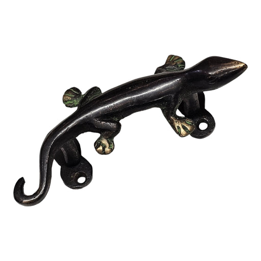 A brass handle in the shape of a gecko lizard with a green patina on a white background