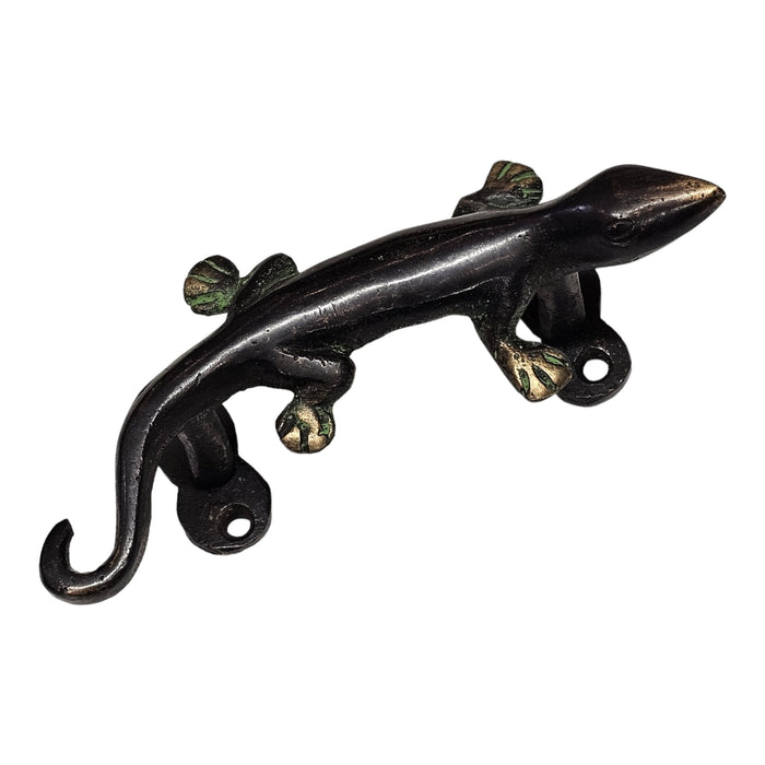 A brass handle in the shape of a gecko lizard with a green patina on a white background