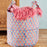 Decorative storage basket with floral pattern and pink tassels on a wooden surface.
