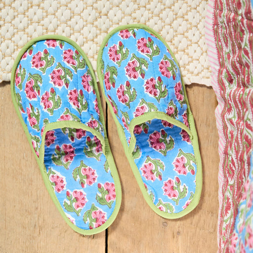 Pair of floral-patterned slippers on a wooden floor with a textured white rug in the background.