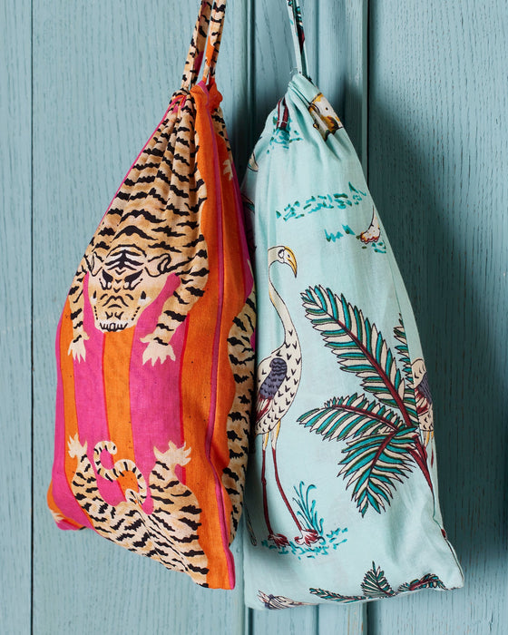 Drawstring bags with tiger print hanging on a wooden surface.