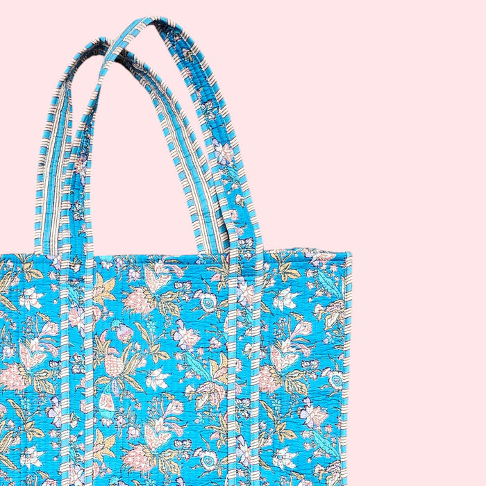 Stap handle detail of a bue cotton quilted tote bag on a soft pink background