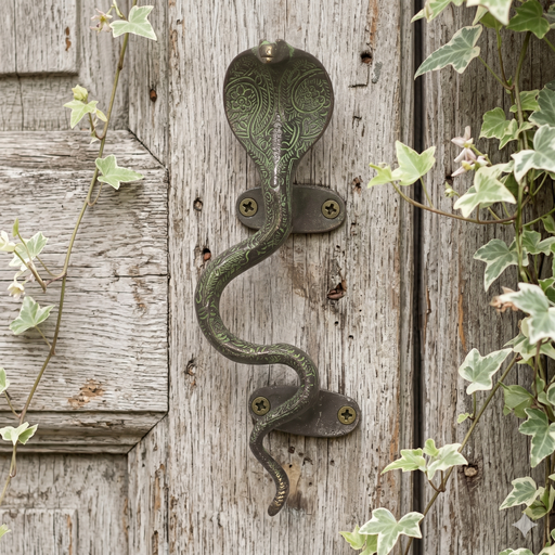 Decorative brass cobra handle with a green patina on a white washed wooden door with ivy leaves