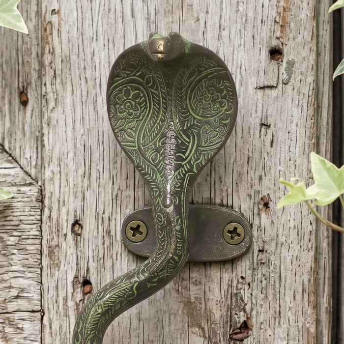 Close up pictaure of a Decorative brass cobra handle with a green patina on a white washed wooden door with ivy leaves.