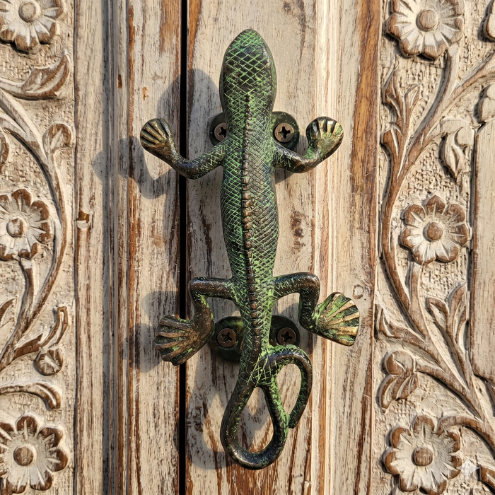 Decorative green metal lizard-shaped handle on a wooden surface with floral carvings